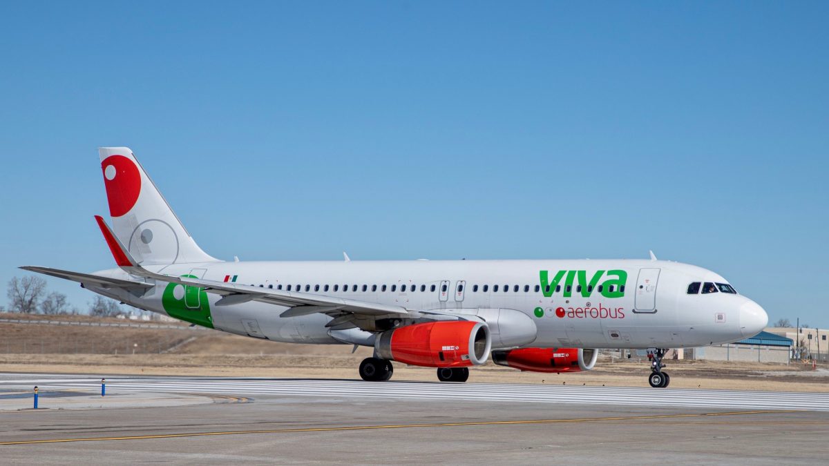 Photo of a white, red, and green plane on a runway with a blue sky in the background