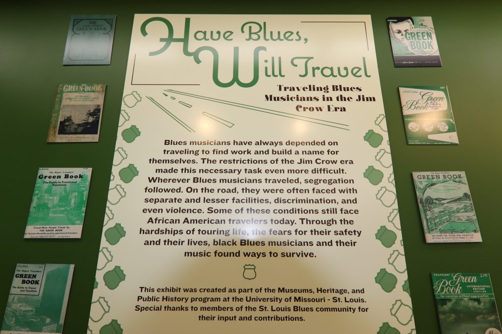 Photo of an art exhibit that says "Have Blues, Will Travel" with a green background.