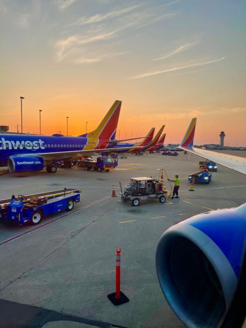Photo of a runway with multicolored planes and a sunset in the background