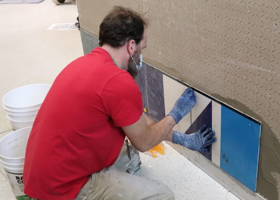 Photo of a man in a red shirt placing a tile on a wall