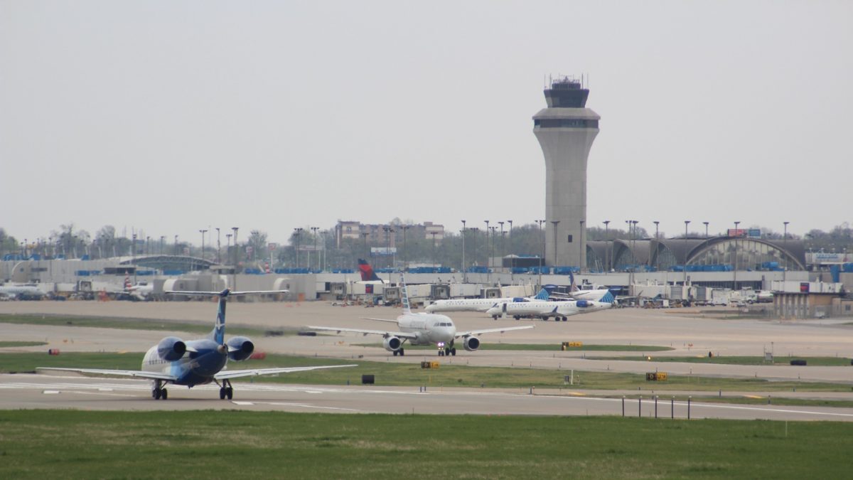 A photo of multiple planes on runways and an airport in the background