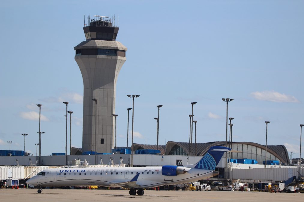 Photo of the outside of an airport with white and blue planes in the foreground