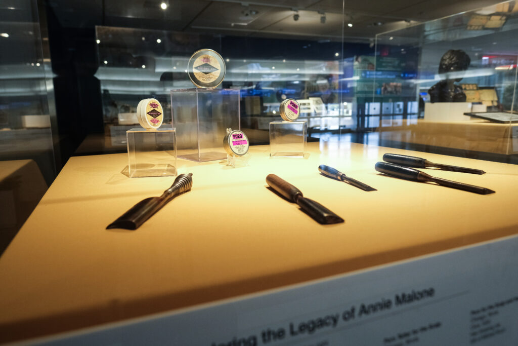 This display case features a collection of vintage Poro beauty products and styling tools. Several small tins of hair and skin products are elevated on clear stands, each labeled with the Poro brand name.