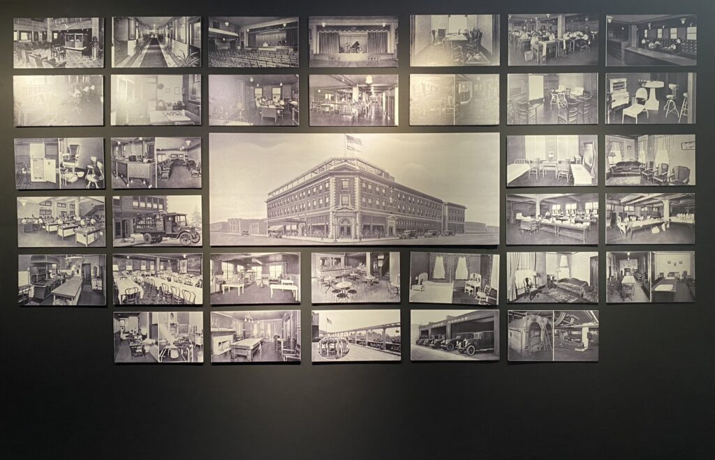 This image shows a wall display of historical photographs depicting various aspects of Poro College, the institution founded by Annie Malone. The centerpiece is a large photograph of the college's exterior, a multi-story building with vehicles parked outside and a flag atop the roof. Surrounding images showcase the interior facilities, including classrooms, dormitories, dining areas, salons, offices, and training spaces.