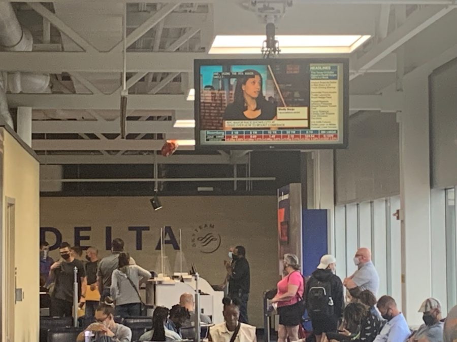 A photo of multiple people in an airport terminal with a television above them