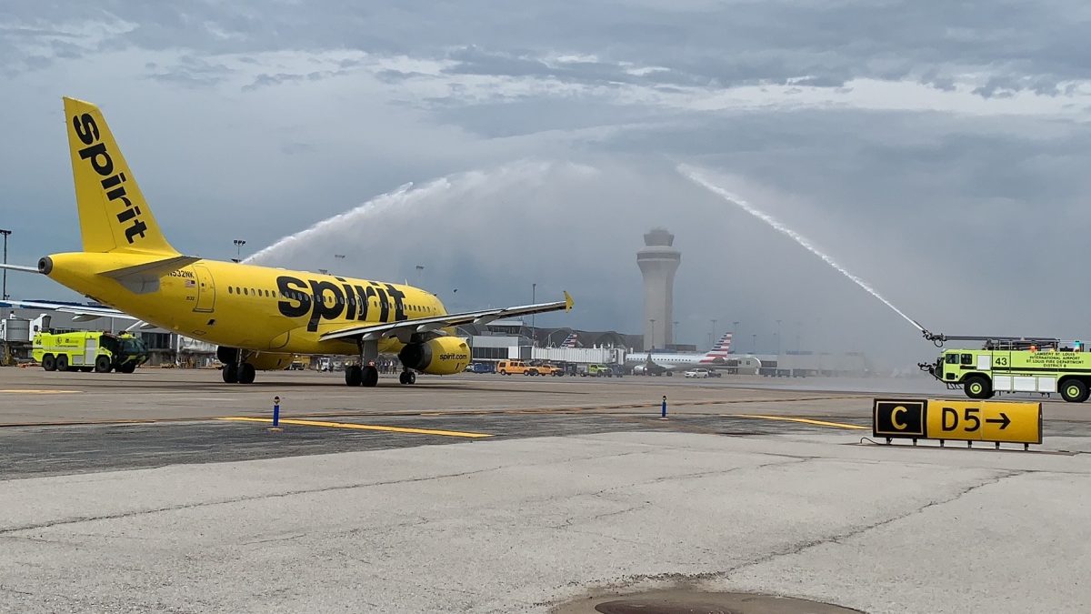 A photo of a yellow Spirit Airlines plane taxiing down a runway with two yellow trucks spraying water