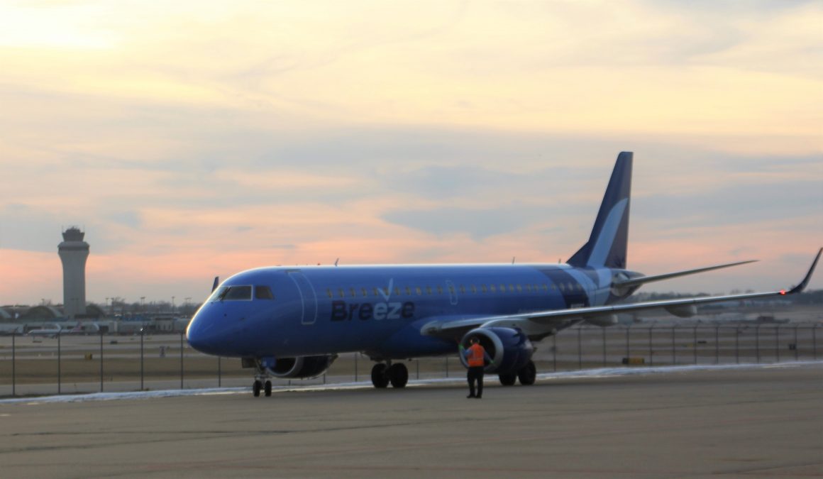 Photo of a blue Breeze plane on a runway with a sunset sky in the background