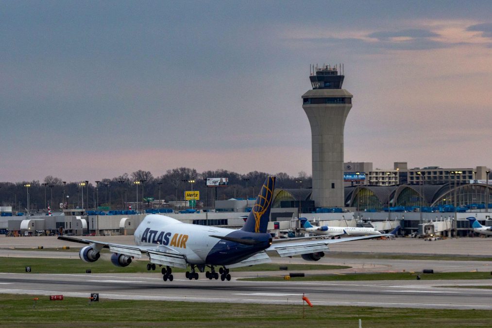 Photo of the back of an Atlas Air plane as it goes down a runway with an airport and airport tower in the background