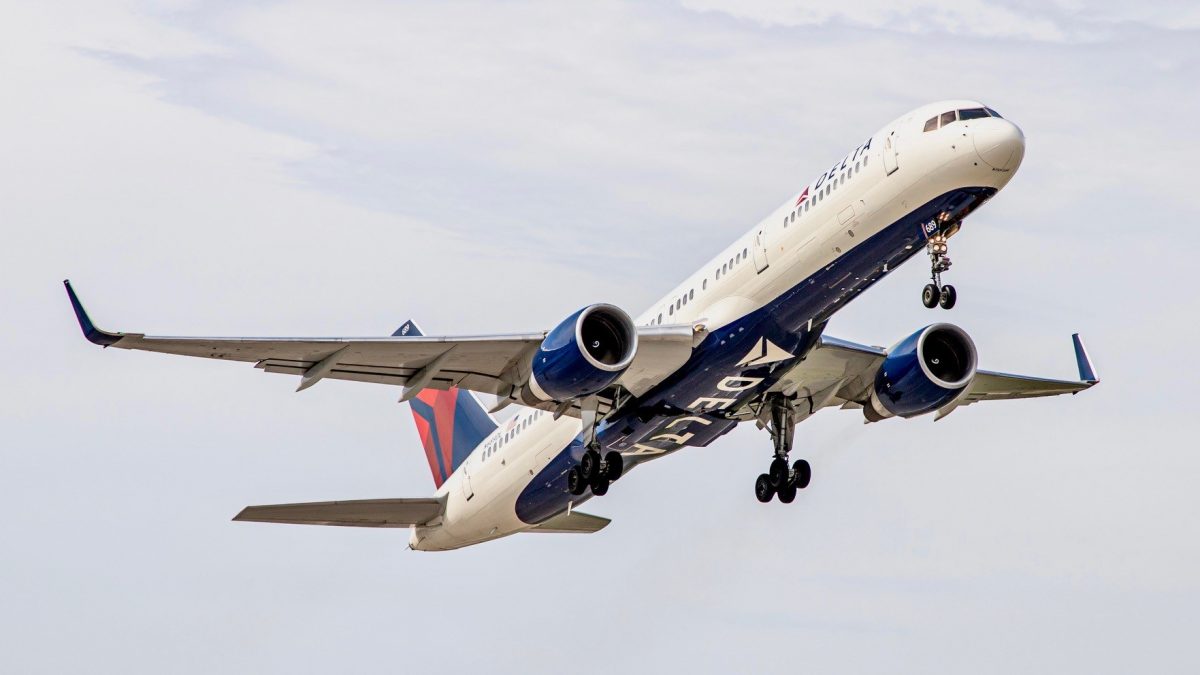 Photo of a Delta Airlines plane in the sky with a white and blue sky behind the plane