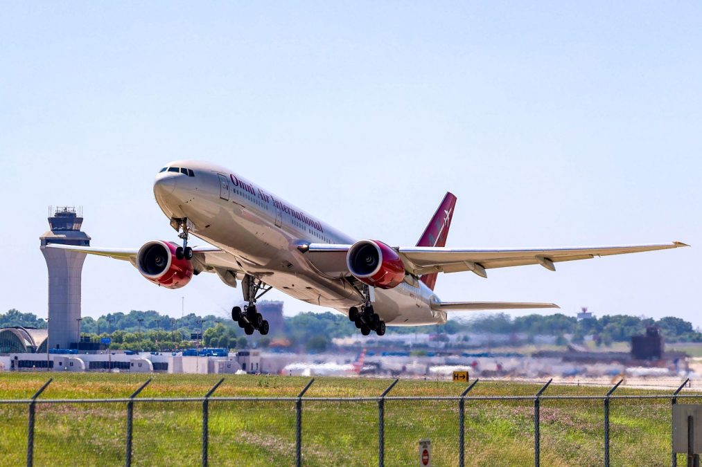 Photo of a Boeing 777-200 from Omni Air International taking off from a runway with an airport in the background