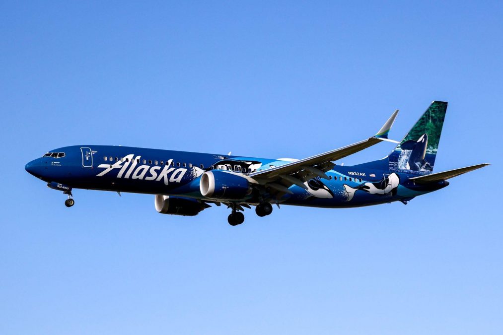 Photo of a blue-colored Alaska Airlines Boeing 737-9 MAX flying against a blue sky
