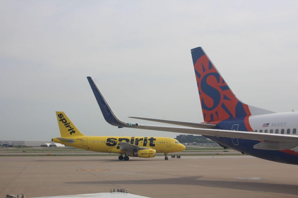 Photo of a yellow Spirit Airlines plane on a runway behind another plane with a red and blue tailfin