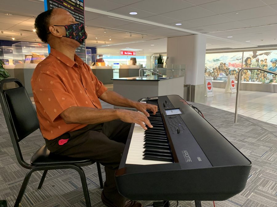 Photo of Ptah Williams playing a keyboard in an airport terminal while wearing an orange patterned shirt