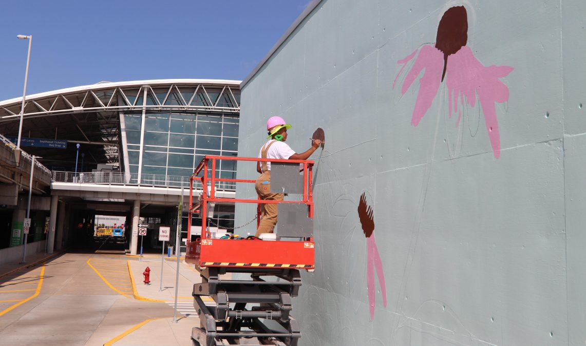 Photo of someone painting pink flowers with brown centers on a large gray wall