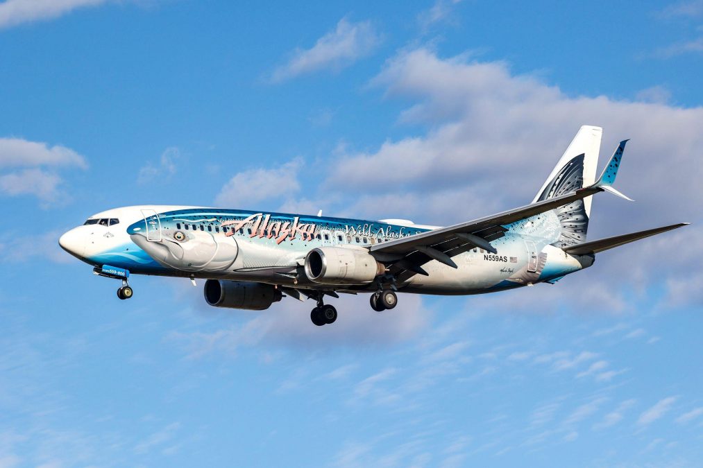 Photo of an Alaskan Airlines plane in the sky with a salmon painted on the side