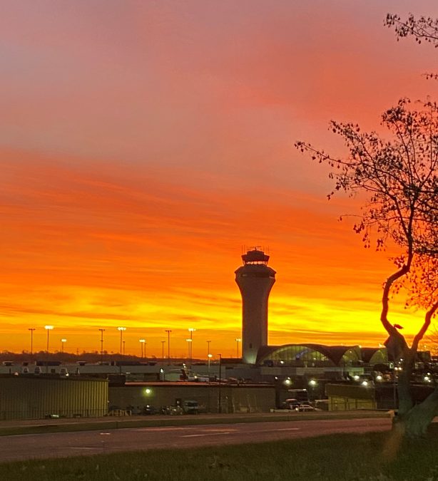 Photo of an orange and red sunrise with an airport tower in front of it