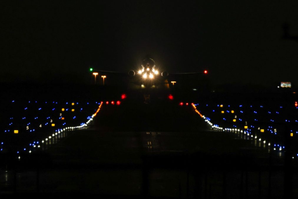 Photo of a plane approaching and a runway full of lights on a dark night.