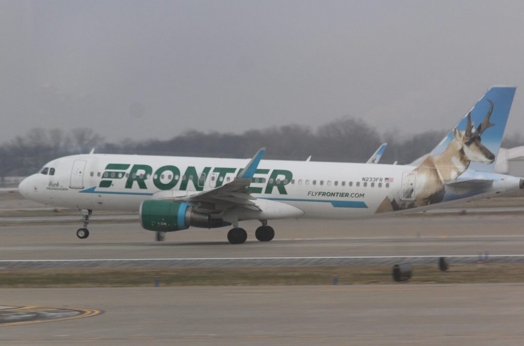 Photo of a white Frontier Airlines plane with green lettering on the side taking off from a runway