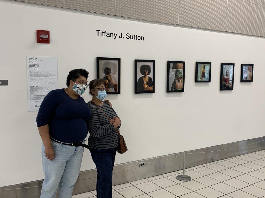 Photo of two people posing in front of a wall with multiple framed photos in a line