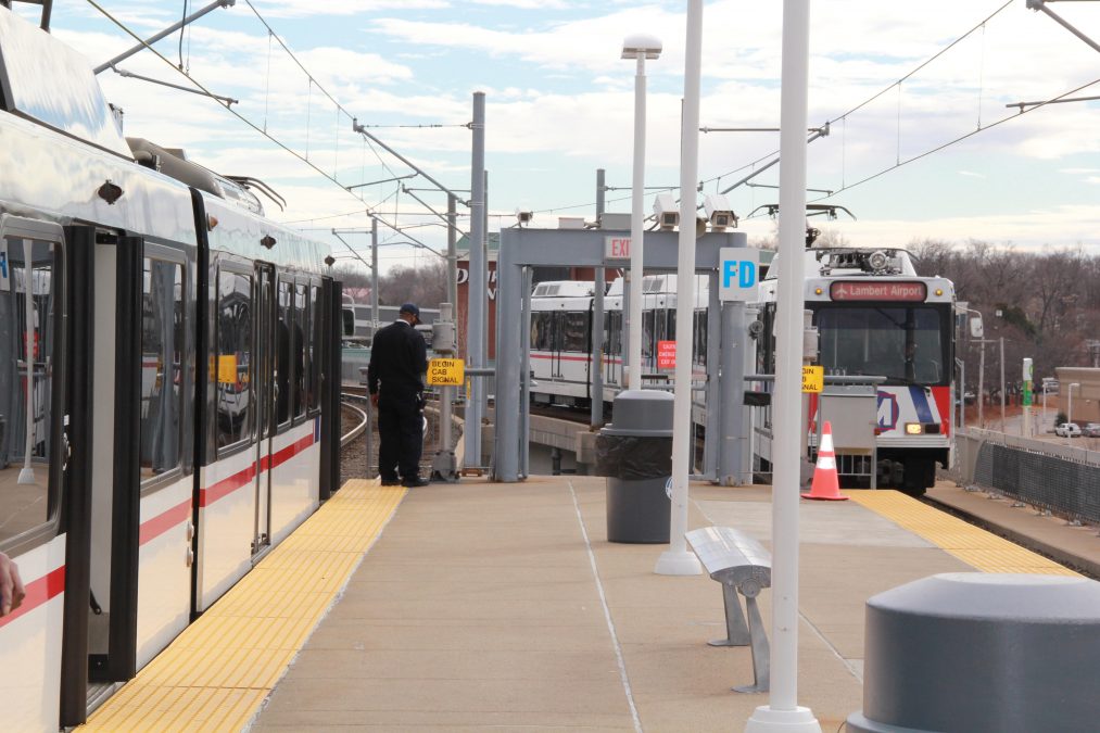 Photo of a train platform with two trains visible and one person standing on the platform