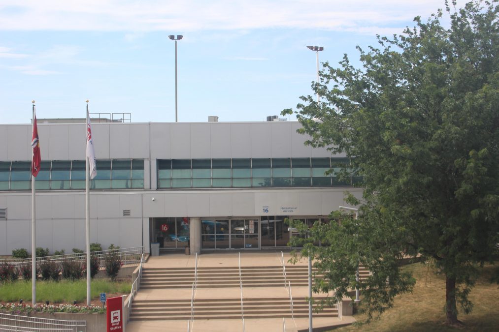 Photo of the outside of a building with two flags flying outside and a tree partially in the foreground