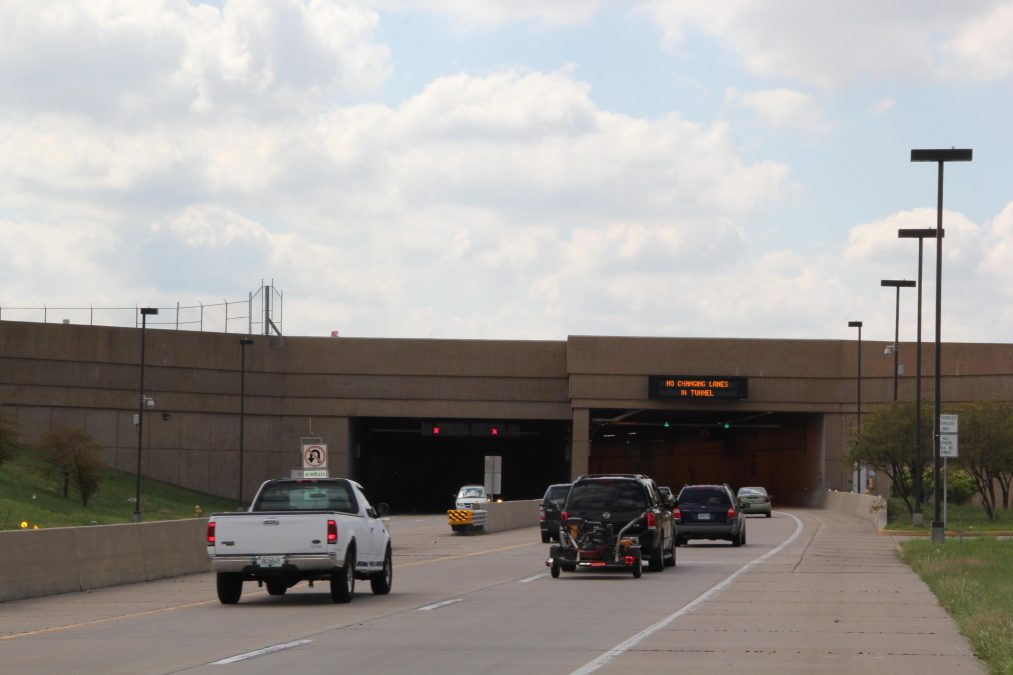 Photo of multiple cars and a truck driving into a tunnel on a road
