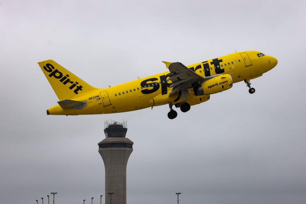 Photo of a yellow Spirit Airlines plane taking off with an airport tower in the background