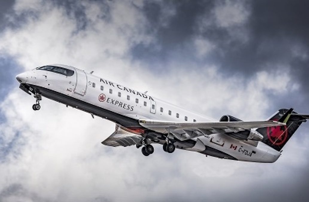 Photo of an Air Canada Express plane flying in the sky against clouds