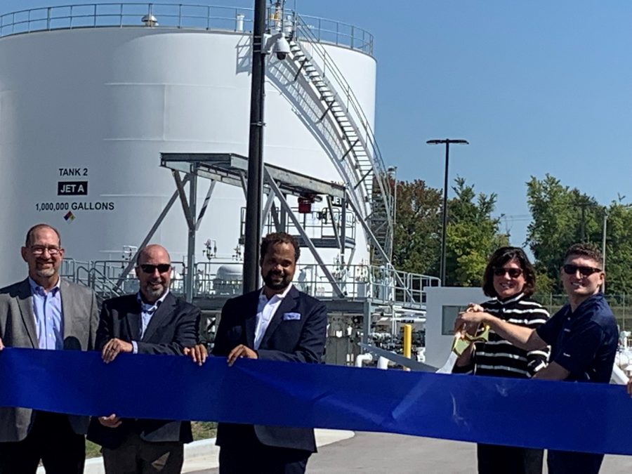 Photo of five people in a line in back of a blue ribbon with two people holding large scissors near the ribbon