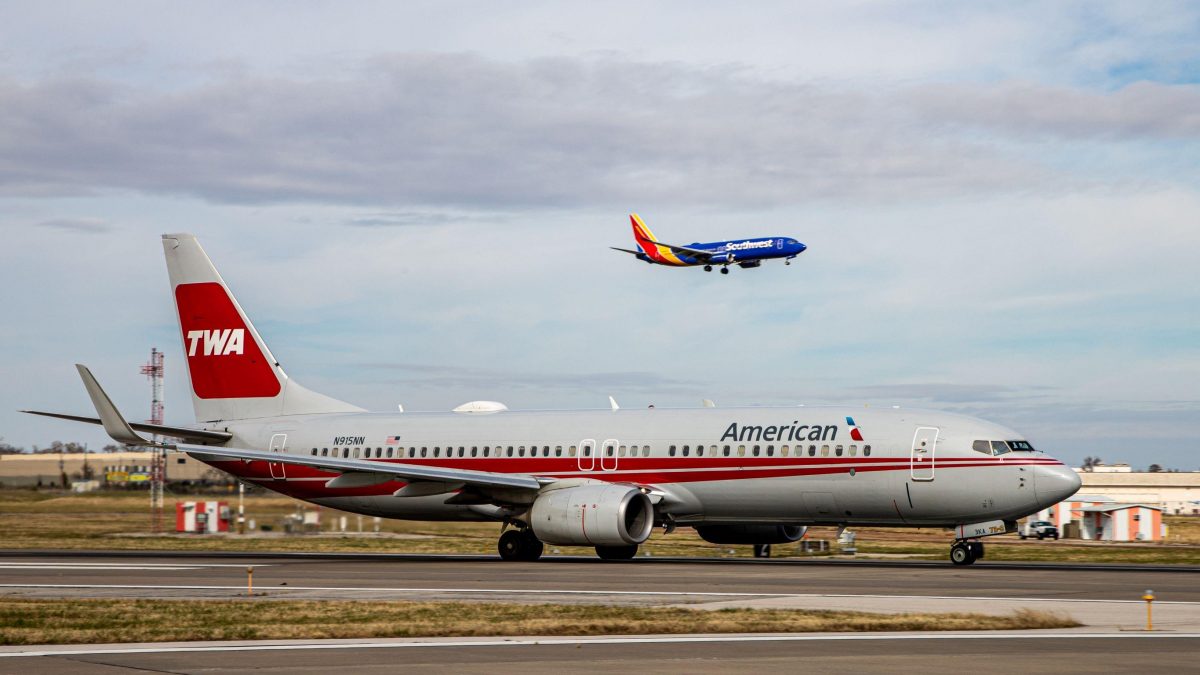 An American Airlines plane sits on the runway awaiting takeoff while a Southwest Airlines plan approaches in the sky.