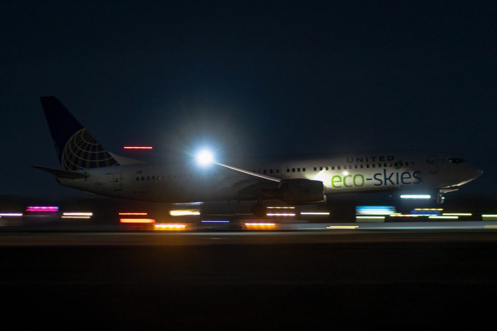 A United Airlines Boeing 737-900 sporting a special livery lands at STL in the dark, the plane illuminated by the wing light and the lights on the runway.