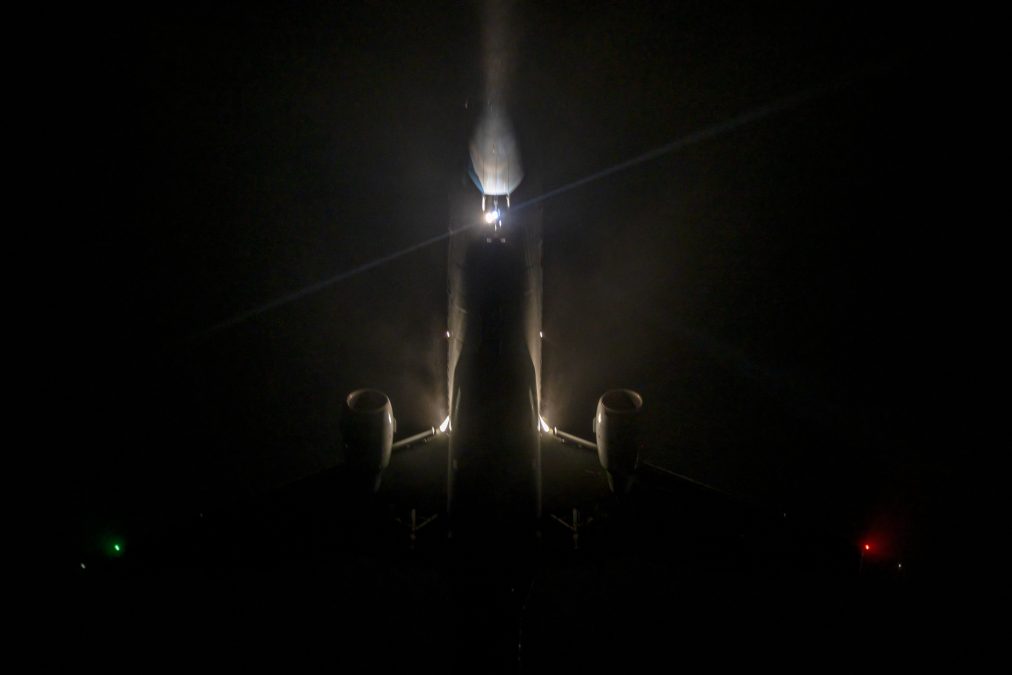 A photo of the underbelly of an E175 plane at night, illuminated by a bright light.
