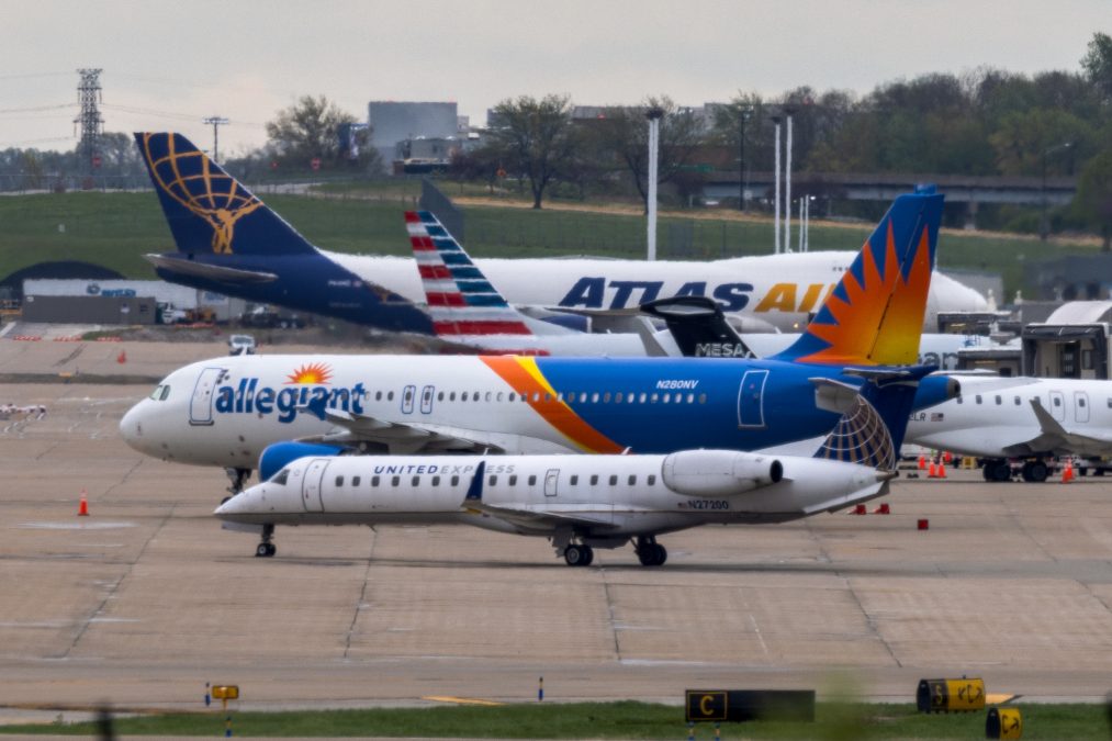 An allegiant airplane moves next to a united express airplane on the ground at STL with many other airplanes in the background.