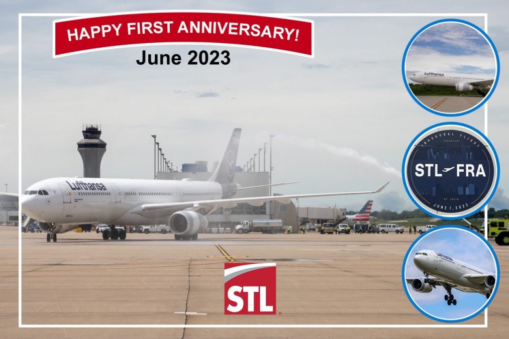 A Lufthansa Airbus A340 is celebrated at St. Louis Lambert International Airport, marking the first anniversary of the STL-FRA (St. Louis to Frankfurt) nonstop route in June 2023. A ceremonial water salute arches over the aircraft in tribute, with the airport's iconic control tower standing tall in the background.
