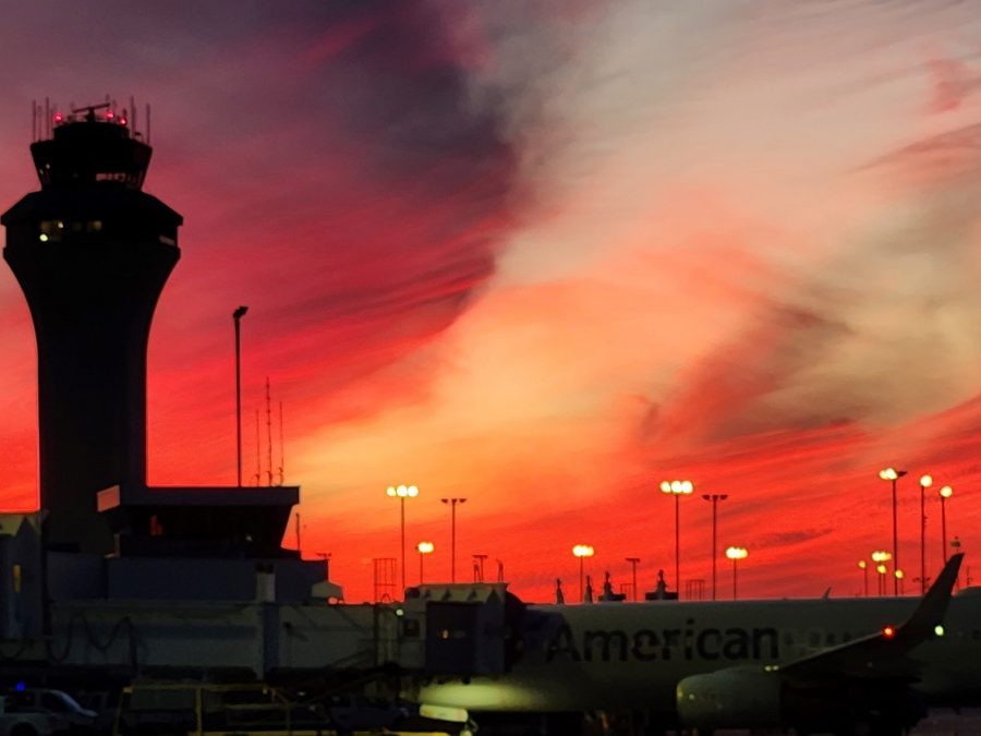 Airport control tower silhouetted against a vibrant red and orange sunset sky.