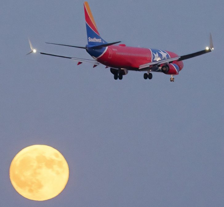 A Southwest airlines plane mid-flight, wrapped with the Tennessee state flag, flies over a full moon.