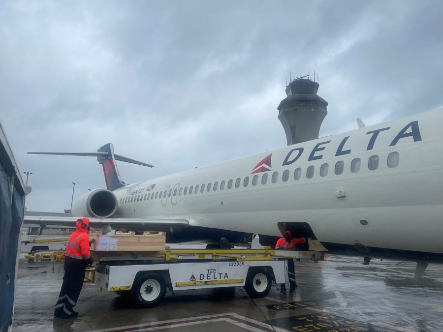 Two workers load a delta airplane with cargo on a rainy day in St. Louis.