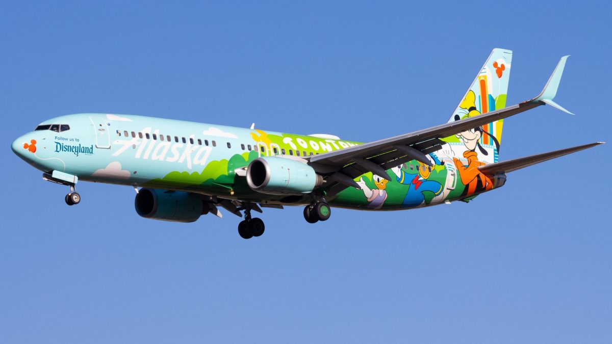 A colorfully painted Alaskan Airlines plane named ToonTown flies in the sky, featuring hand painted artwork of Daisy Duck, Donald Duck and Goofy.