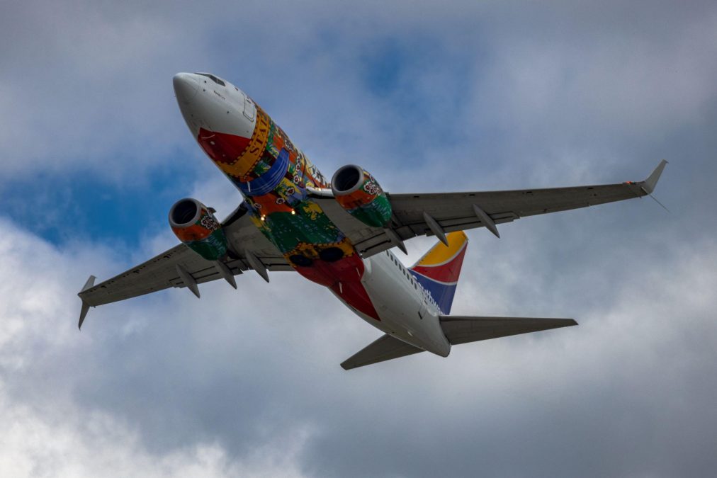 Photo showing a Southwest Airlines Florida One plane in the air with a multitude of colors on the underbelly of the plane.
