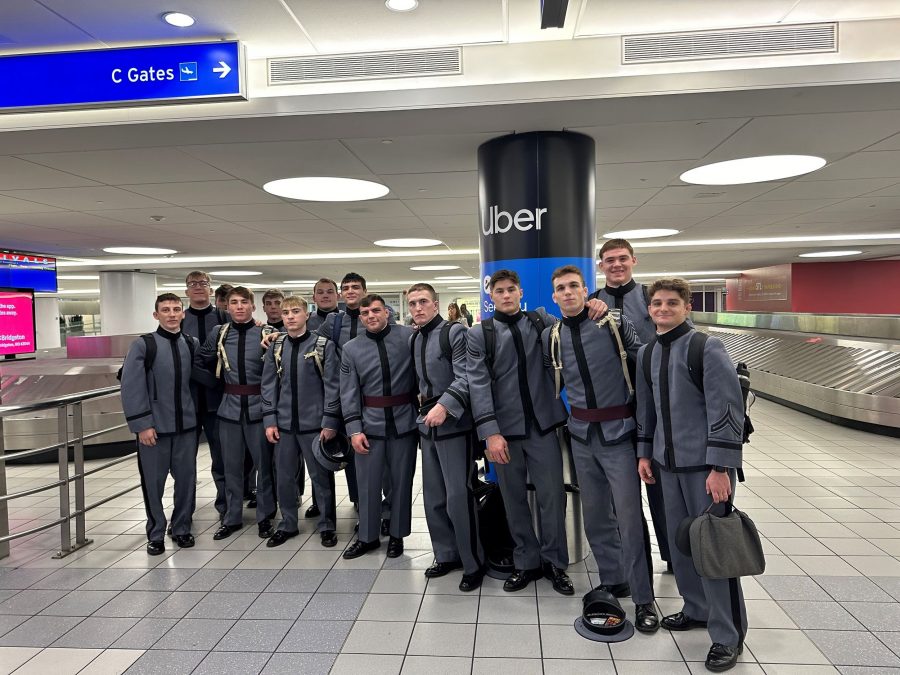 A group of West Point cadets, dressed in formal gray uniforms, pose together at St. Louis Lambert International Airport near the baggage claim area.