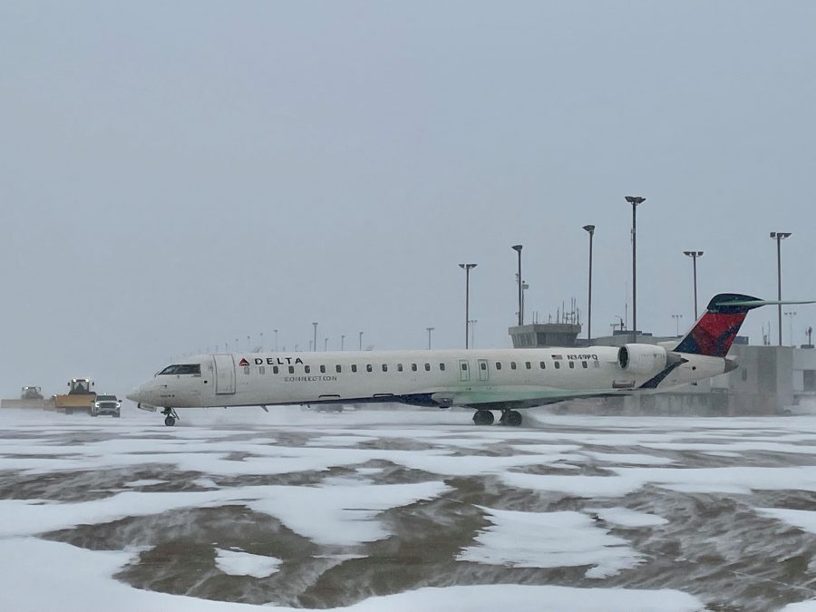 A delta plane sits on the runway while crews work to plow snow on the ground.