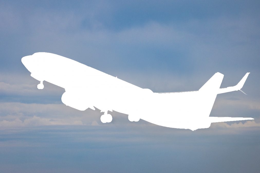 An edited image featuring the silhouette of an airplane over a cloudy sky. The plane's shape is blanked out in white, creating a contrast with the blue and gray clouds in the background.