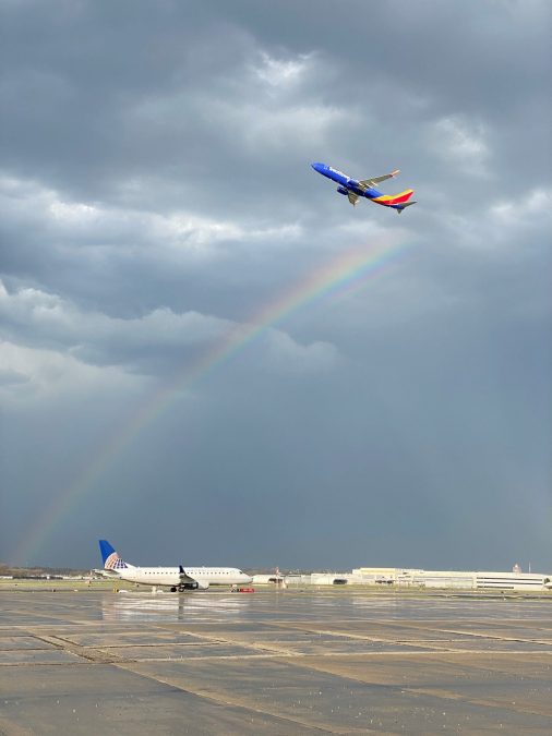 A Southwest Airlines plane flies in the sky with a rainbow below on a rainy day.