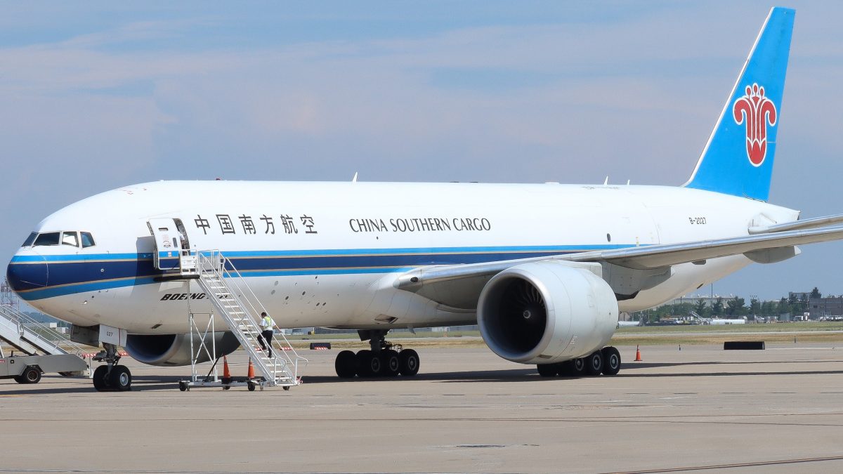 A China Southern Cargo plane is parked on the tarmac with a stair ramp leading up to its open side door. The aircraft features a blue and white color scheme, with Chinese characters and the airline's name displayed on the fuselage. Ground crew and equipment are positioned nearby.