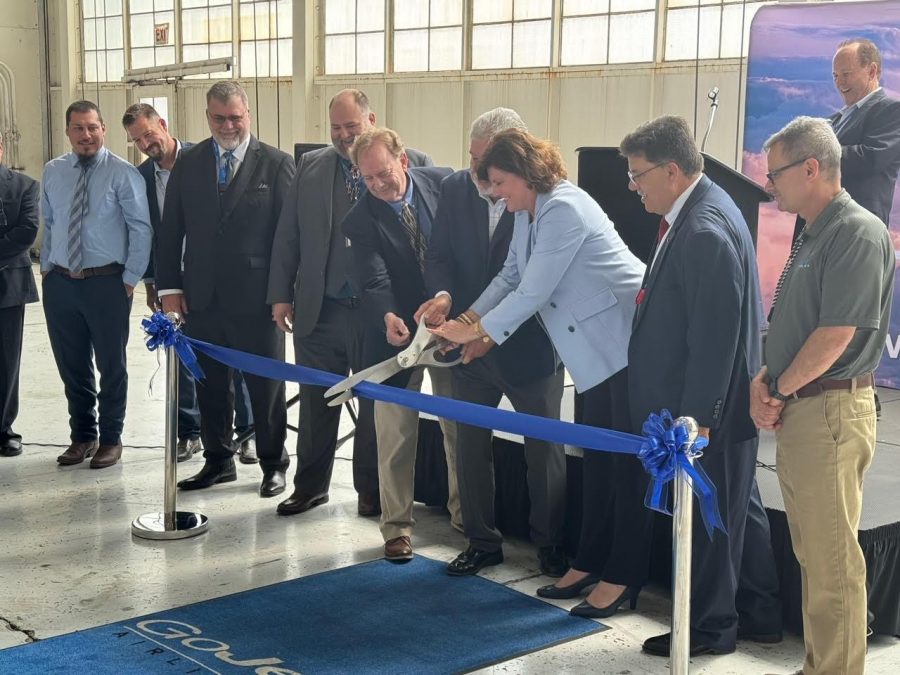 At the ribbon-cutting ceremony for GoJet Airlines, St. Louis Lambert International Airport Director and CEO Rhonda Hamm-Niebruegge and GoJet President and CEO Rick Leach jointly cut a blue ribbon with ceremonial scissors. They are surrounded by other officials and executives, who observe the moment with smiles. The event takes place indoors, with a blue carpet and ribbon stands marking the occasion.