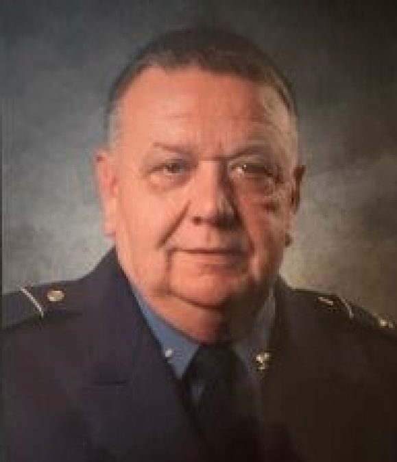 Retired St. Louis Lambert International Airport Police Chief Paul Mason is pictured in formal attire, with a distinguished expression. The portrait features him in a dark uniform with silver insignias on the collar, symbolizing his leadership and service to airport security operations.