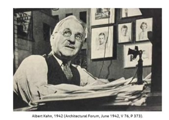 Black-and-white photograph of Albert Kahn, a prominent American industrial architect, taken in 1942. Kahn, an older gentleman with round glasses and neatly combed hair, is seated at a desk piled high with papers. He wears a vest over a white dress shirt with rolled-up sleeves and a patterned tie. He is looking off to the side with a thoughtful expression. Behind him, several framed portrait photographs are hung on the wall. A vintage telephone with a separate mouthpiece and earpiece sits on the desk. The image was originally published in the Architectural Forum in June 1942.
