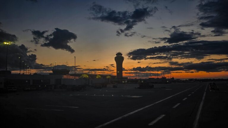 Twilight photograph of St. Louis Lambert International Airport’s airfield, featuring a dramatic sky with deep orange and blue hues as the sun sets behind scattered clouds.