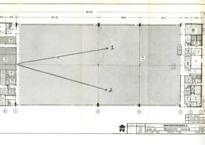 Architectural floor plan labeled MCDONNELL, showing a large central hangar space with two arrows labeled 1 and 2 pointing to specific locations in the hangar; surrounding rooms and details are visible.