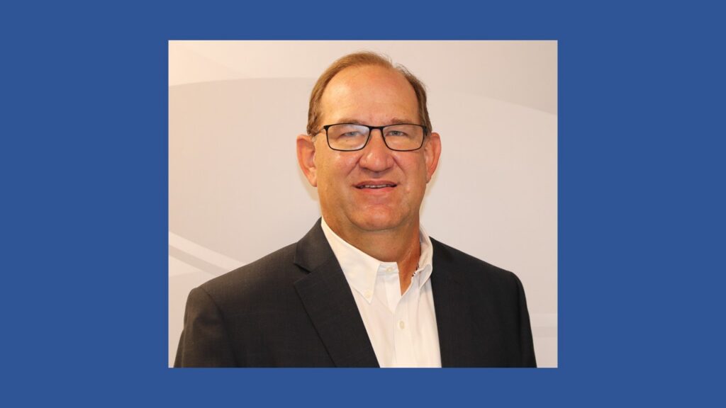 This is a portrait photo of Gerald Beckmann. He is framed in front of a gray background in a dark suit with an open collared white shirt. He will become St. Louis Lambert International's Interim Airport Director on August 16, 2026.